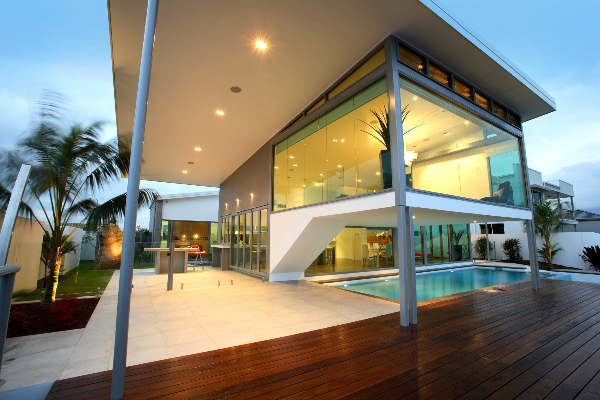 Glass-walled home above a pool and timber deck at dusk
