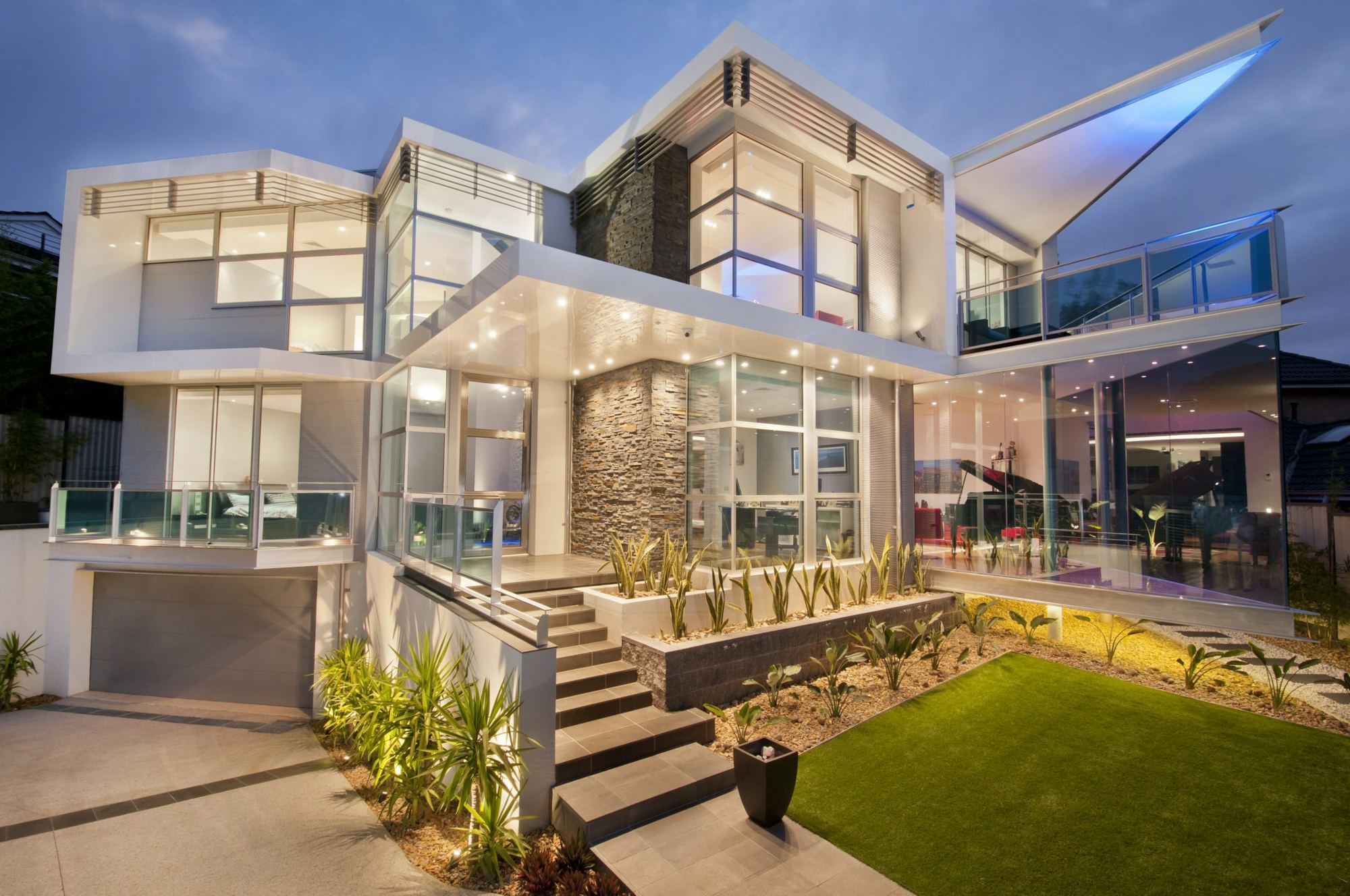 Architectural DRH home with glass balconies and a stone feature wall at dusk
